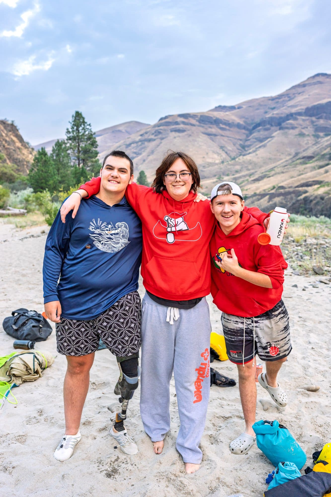 Three people posing together outdoors with hills in the background
