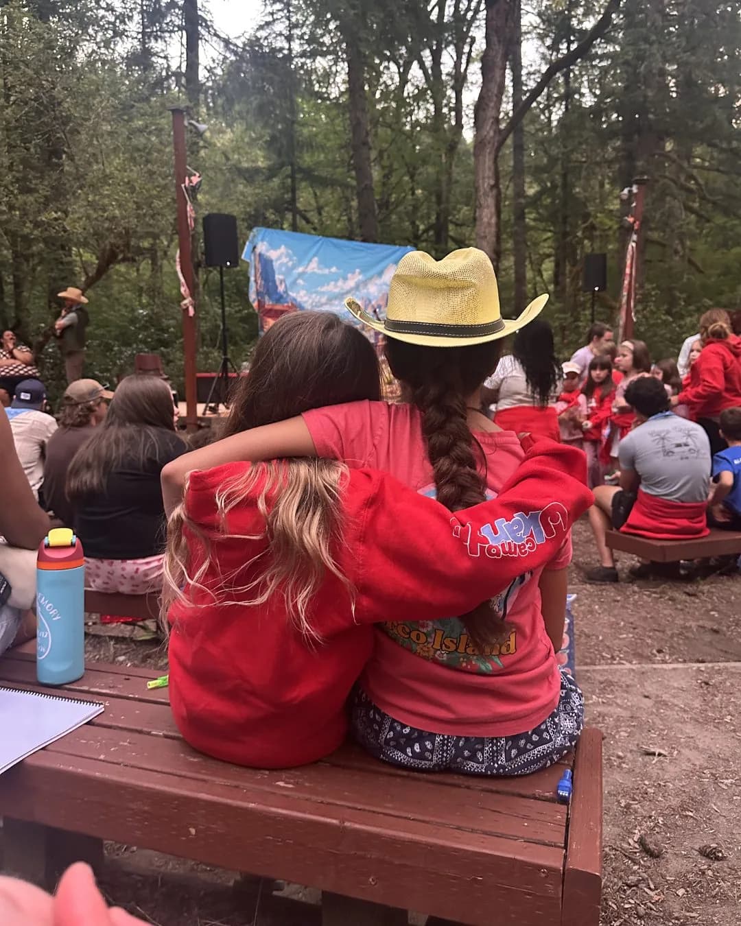 The backs of two campers with their arms around each other at campfire